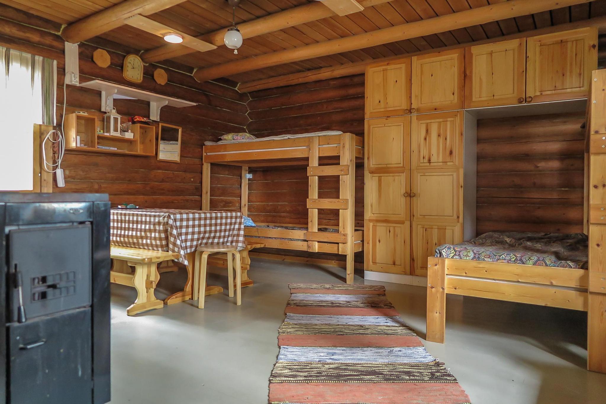 Scenic view of a property featuring two cabins on a narrow peninsula by Lake Saarivesi, with a shallow, sandy beach and private dock. The main cabin, built in 1995, includes a covered porch and separate sleeping quarters. Adjacent is a sauna cabin built in 2012, with an upper sleeping loft and a sauna accessible by steep stairs. Amenities include a grill shelter, cold cellar, and a rowboat. The lush, tree-lined surroundings emphasize a serene, secluded retreat ideal for relaxation and enjoying nature