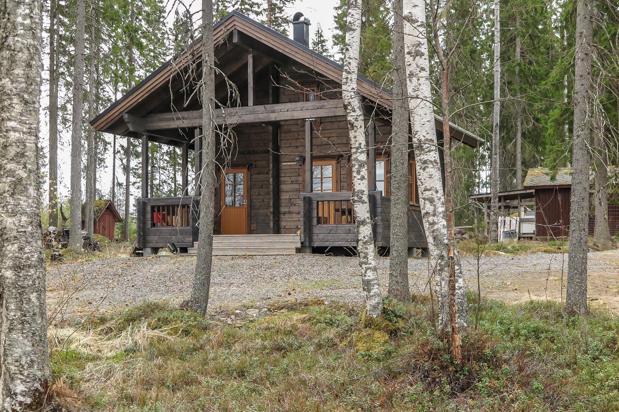 Scenic view of a property featuring two cabins on a narrow peninsula by Lake Saarivesi, with a shallow, sandy beach and private dock. The main cabin, built in 1995, includes a covered porch and separate sleeping quarters. Adjacent is a sauna cabin built in 2012, with an upper sleeping loft and a sauna accessible by steep stairs. Amenities include a grill shelter, cold cellar, and a rowboat. The lush, tree-lined surroundings emphasize a serene, secluded retreat ideal for relaxation and enjoying nature